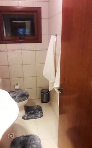 Ett badrum med en toalett, en liten papperskorg, en handduk som hänger på väggen och ett fönster med träram.