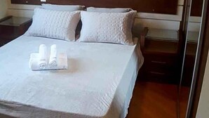 Un lit bien fait, avec un couvre-lit blanc et des oreillers, une tête de lit en bois et une table de chevet avec une lampe.