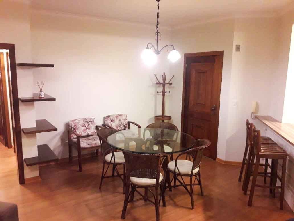 A dining area with a round glass table surrounded by four chairs, a wooden coat rack, and a wooden door.