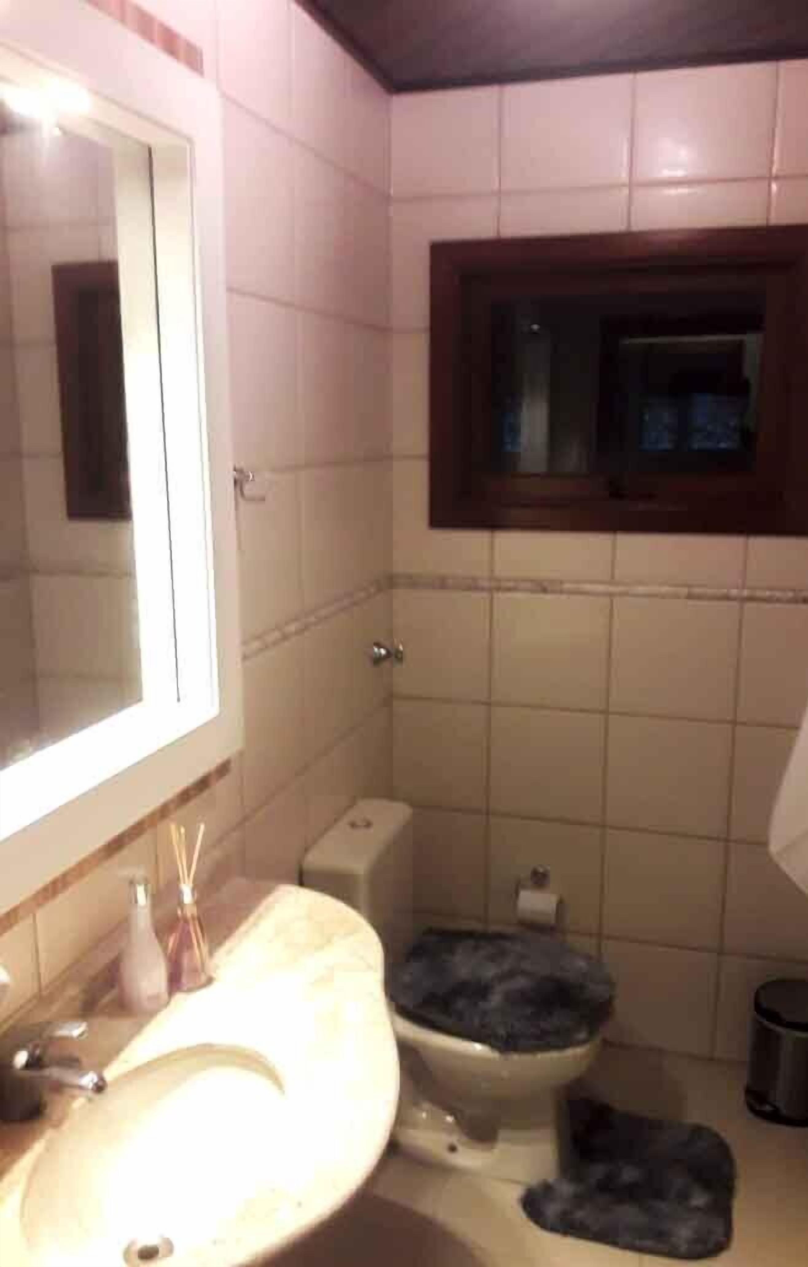 Un baño con lavamanos, espejo, inodoro y una ventana sobre el inodoro.