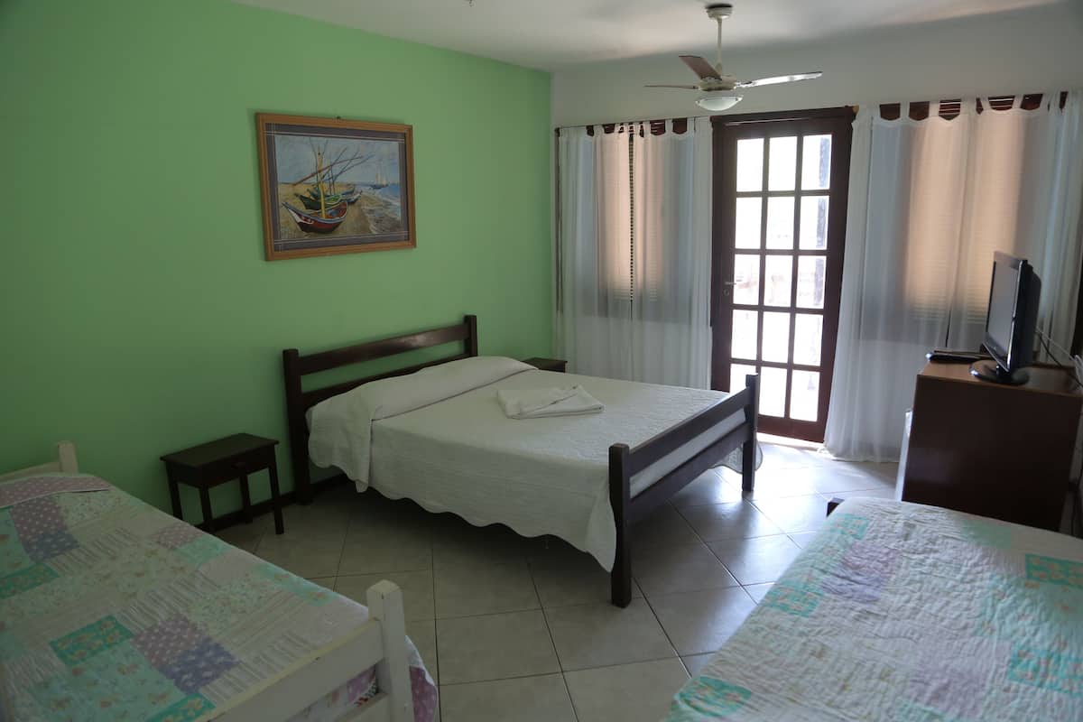 A bedroom with a single bed, a small bedside table, a nightstand, a television, and a window with curtains.