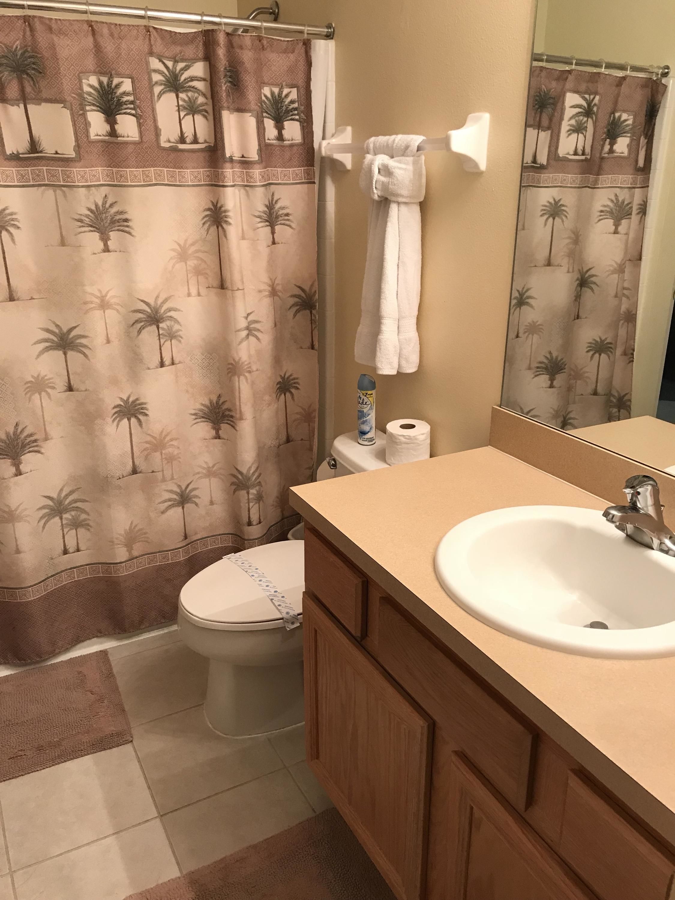 A bathroom with a toilet, a sink, a towel rack, and a shower curtain with palm tree patterns.