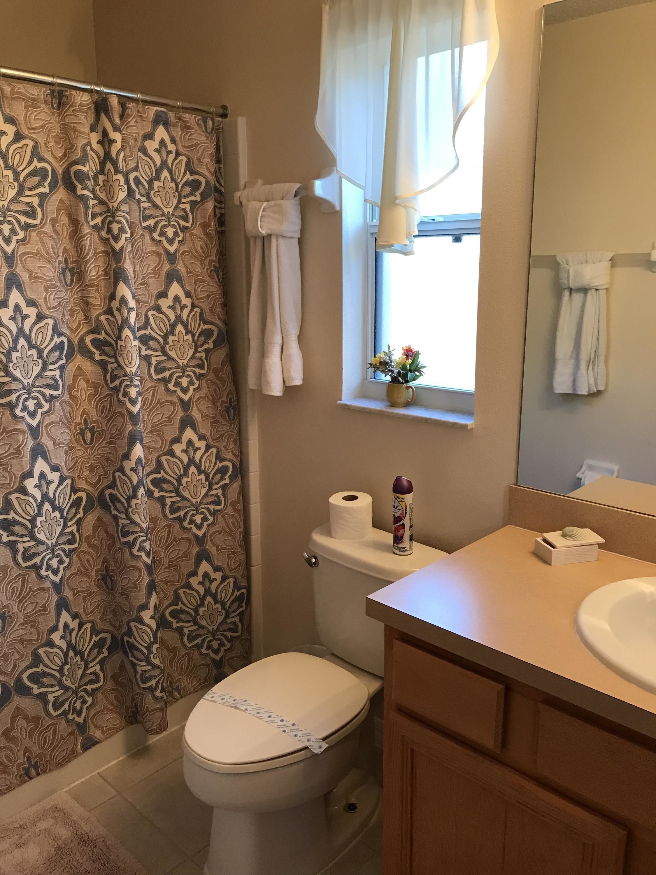 Un baño con inodoro, lavabo, cortina de ducha y ventana, con una toalla colgada en la pared.