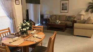 Ein Wohnzimmer mit Esstisch für zwei Personen, einer Couch, einem Couchtisch und einem Fernseher.