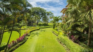Un sendero exuberante en un jardín con palmeras y césped cuidado, que conduce a un edificio con balcones.