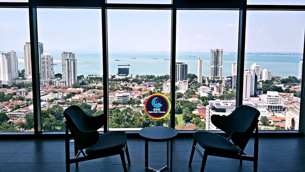 A room with large windows overlooking a cityscape and water. There are two chairs and a small table. - 10Pax Designer Suite - Georgetown Penang (George Town)