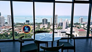 A table with chairs in front of large windows overlooking a cityscape with buildings and a body of water. - 10Pax Designer Suite - Georgetown Penang (George Town)