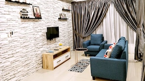 A modern living room with a brick-patterned wall, a flat-screen TV mounted above a wooden TV stand, a blue sofa with a Union Jack pillow, and a ceiling fan. - 10Pax Designer Suite - Georgetown Penang (George Town)