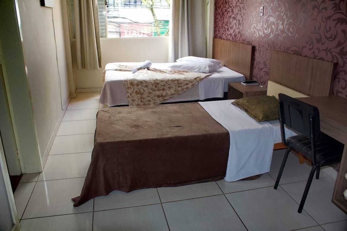 Habitación de hotel con dos camas, un escritorio, una silla y un ventanal con cortinas.