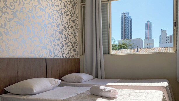 Hotelkamer met drie bedden, behang met een patroon, uitzicht op stadsgebouwen en een raam met gordijnen.