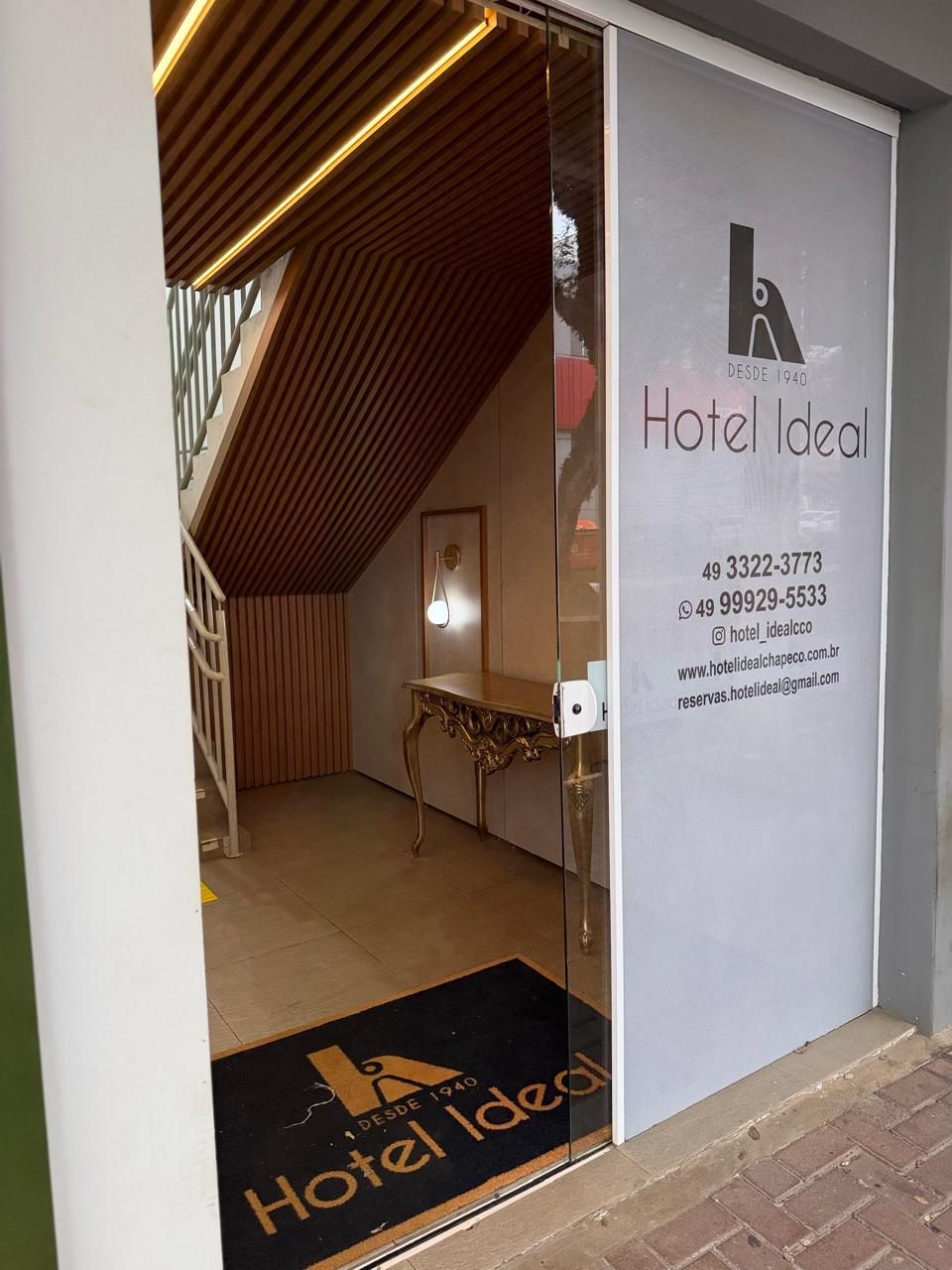 A hotel entrance with a modern design, including a wooden sloped ceiling and a glass door.