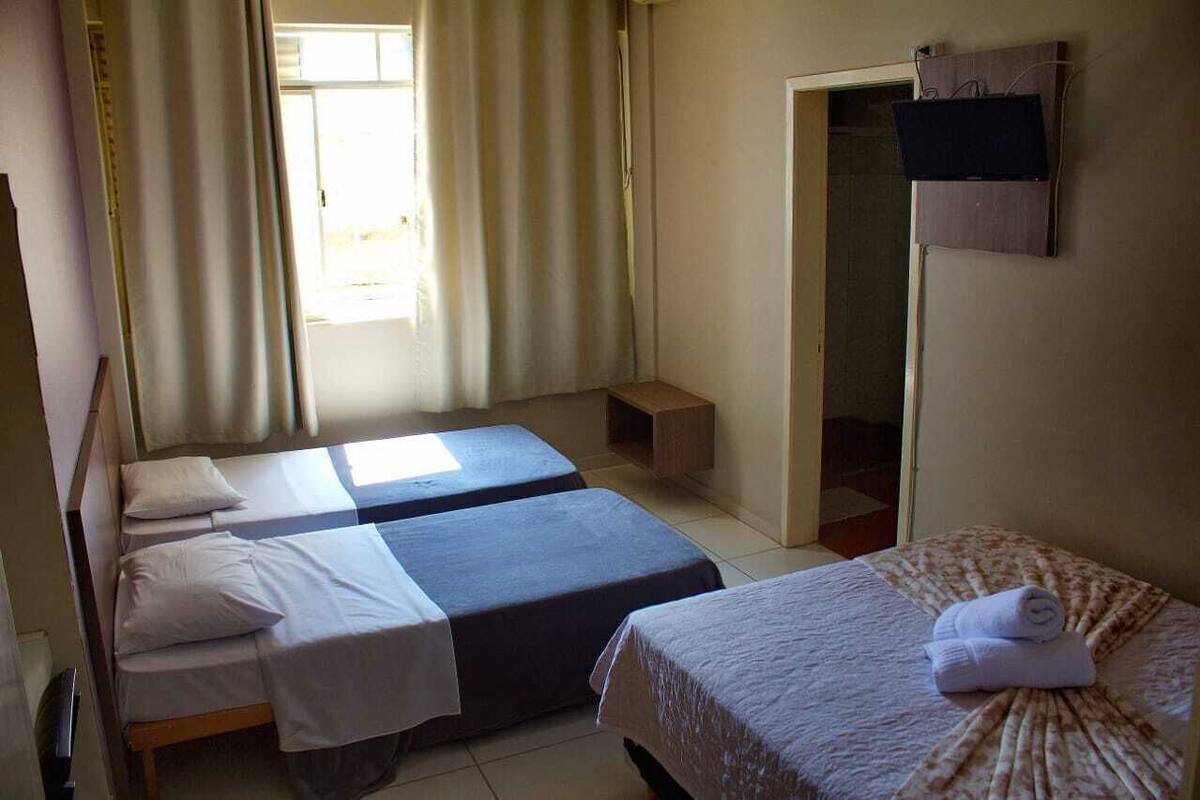 Una habitación con dos camas, un pequeño estante de madera, un televisor montado en la pared y una puerta que da a otra habitación.
