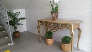 Een trap met een metalen leuning, een decoratietafel met twee potplanten, en een behang met patroon op de achtergrond.