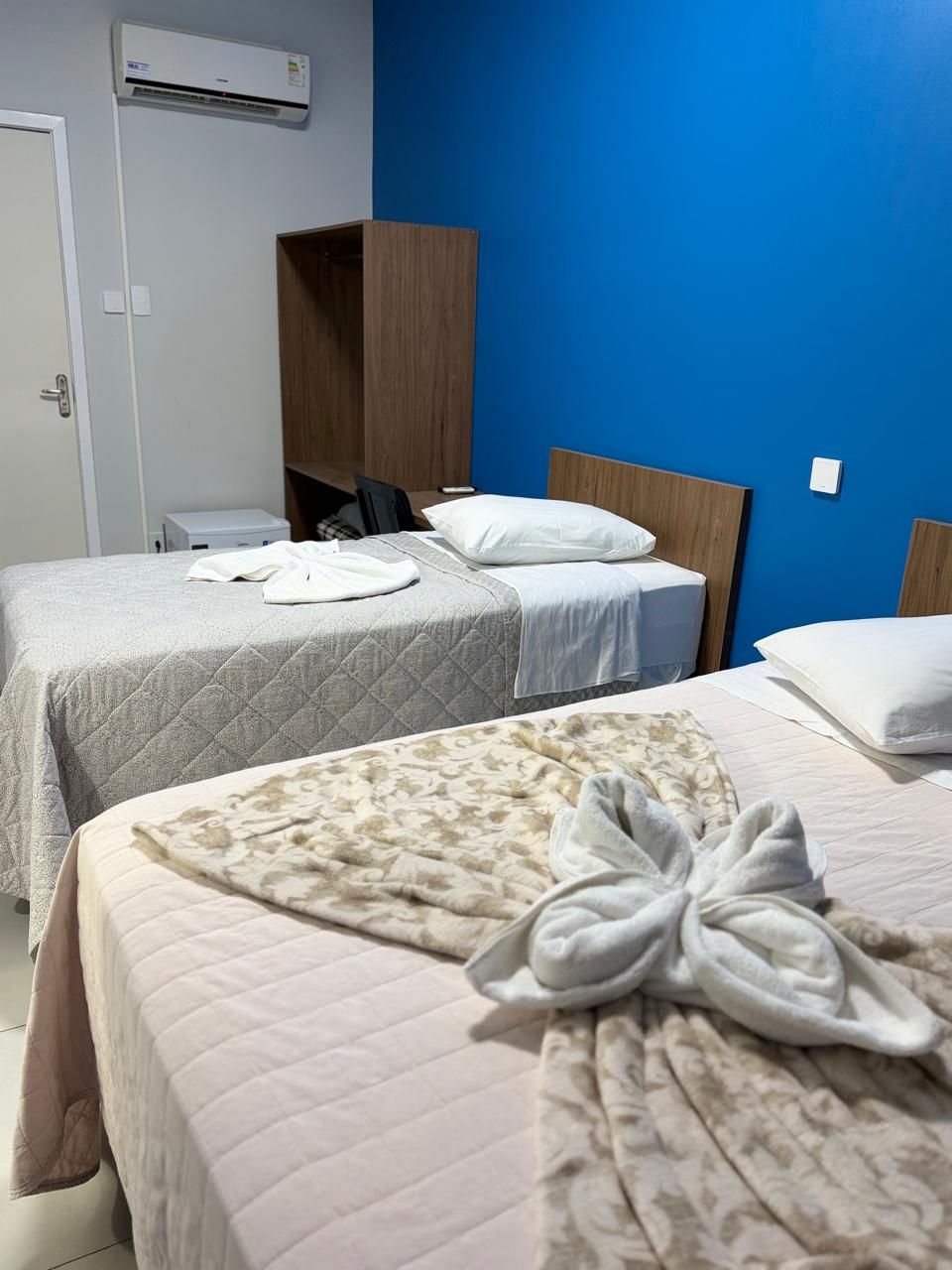 A hotel room with two beds, a wardrobe, and an air conditioning unit.