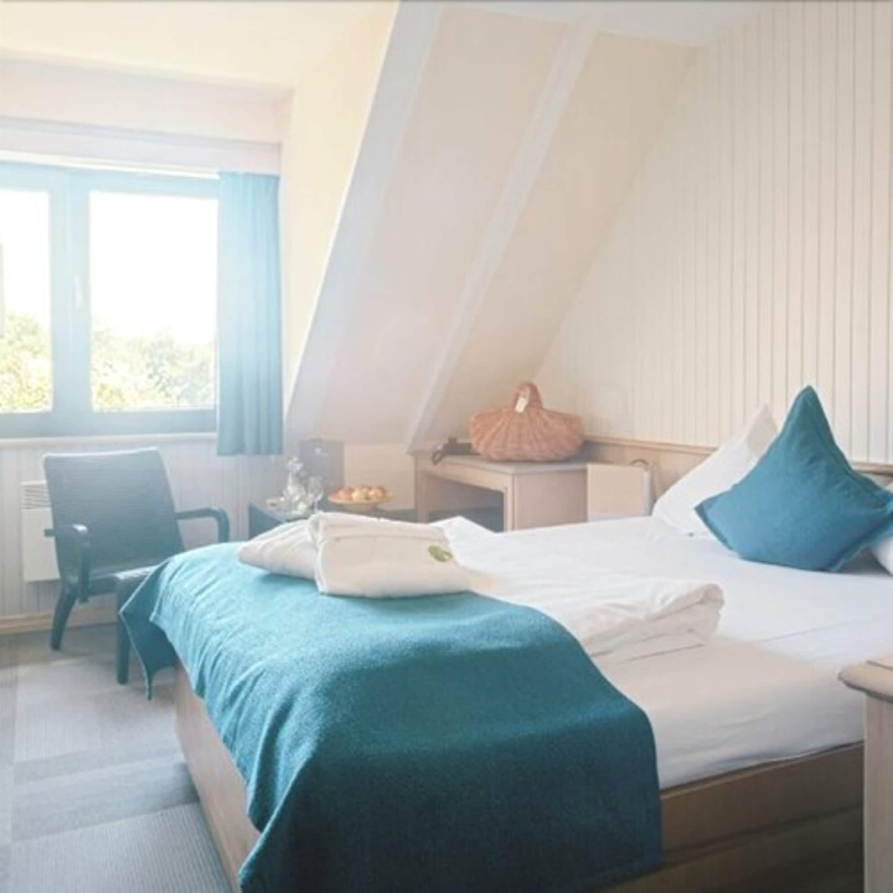 A bedroom with a bed, a chair, a nightstand, and a window.