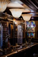 A bar area with hanging lamps, a stained glass window, and various bar equipment.