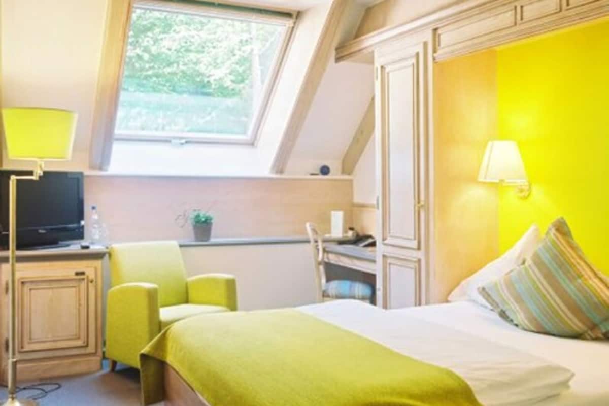 A room with a bed, a desk, a chair, a TV, and a window.