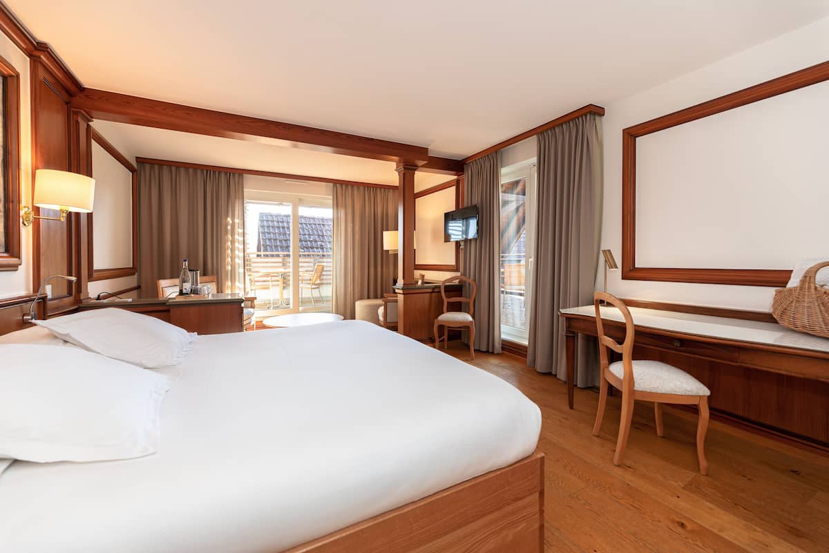 A hotel room with a large bed, a desk, a chair, a television, and a window with curtains.