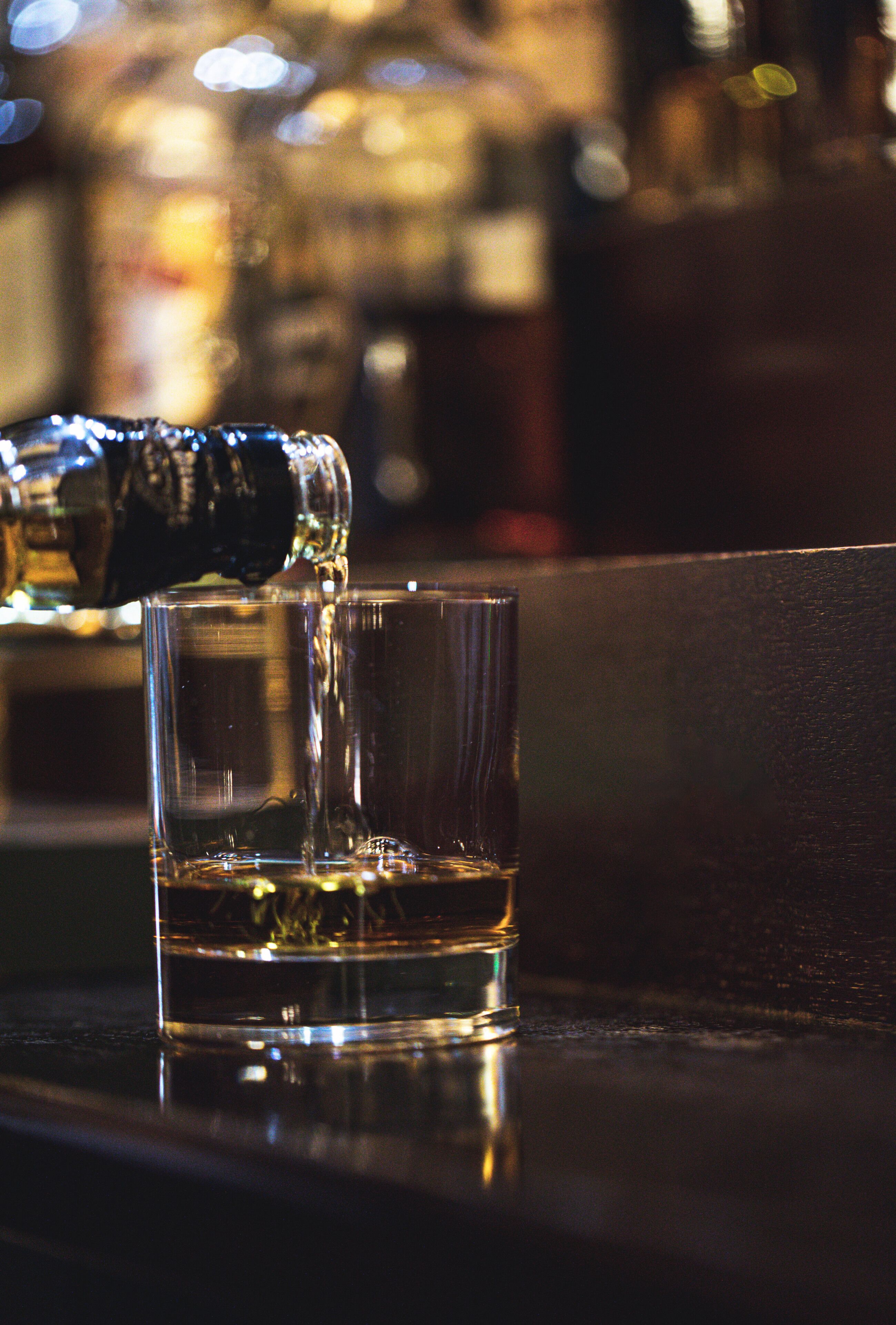 A glass being filled with a dark liquid, likely a beverage, on a reflective surface.