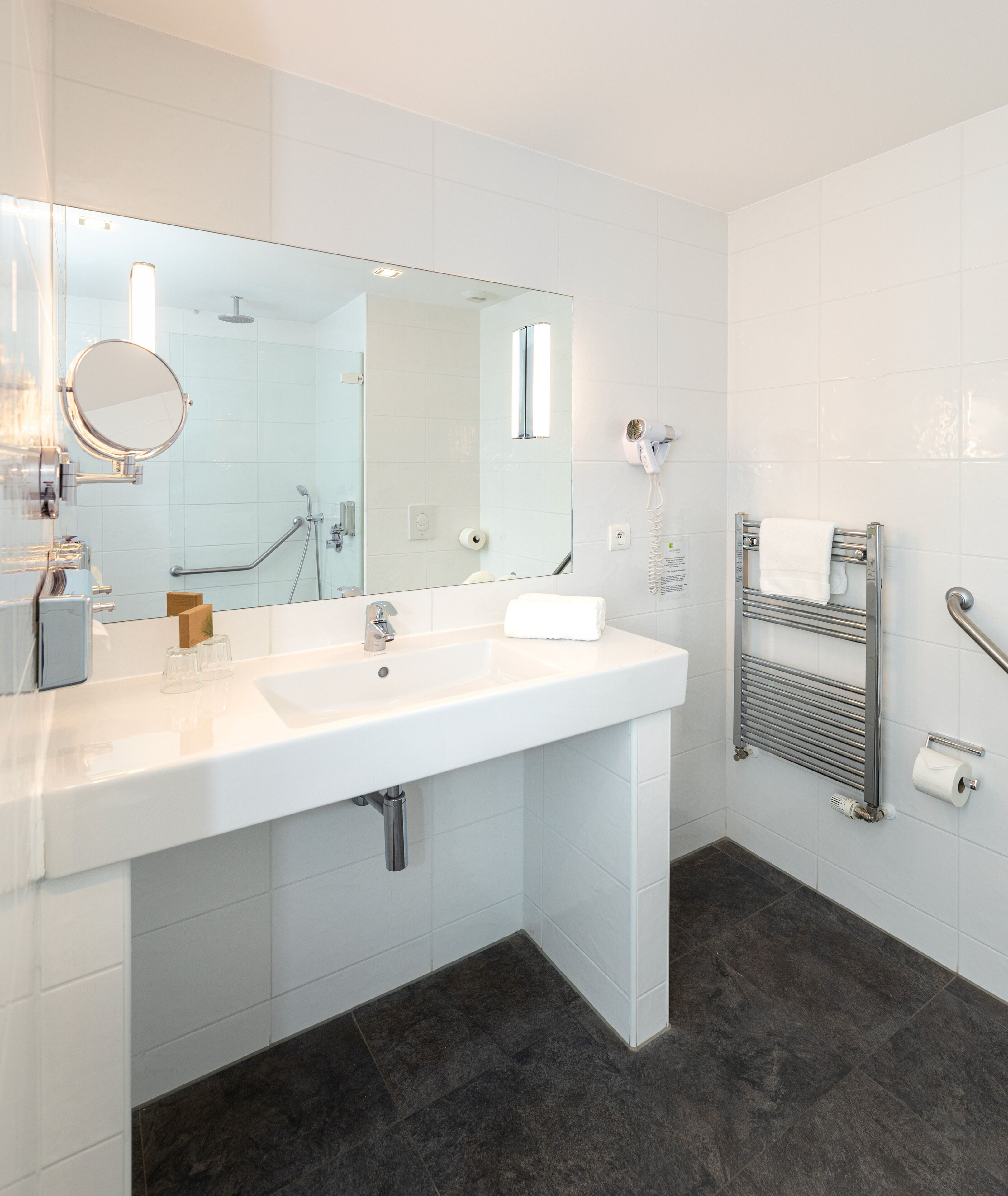 A modern bathroom with a white sink, large mirror, and a towel rack.