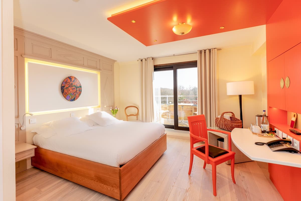 A hotel room with a wooden bed, a desk with a chair, a large window, and a view of the outdoors.