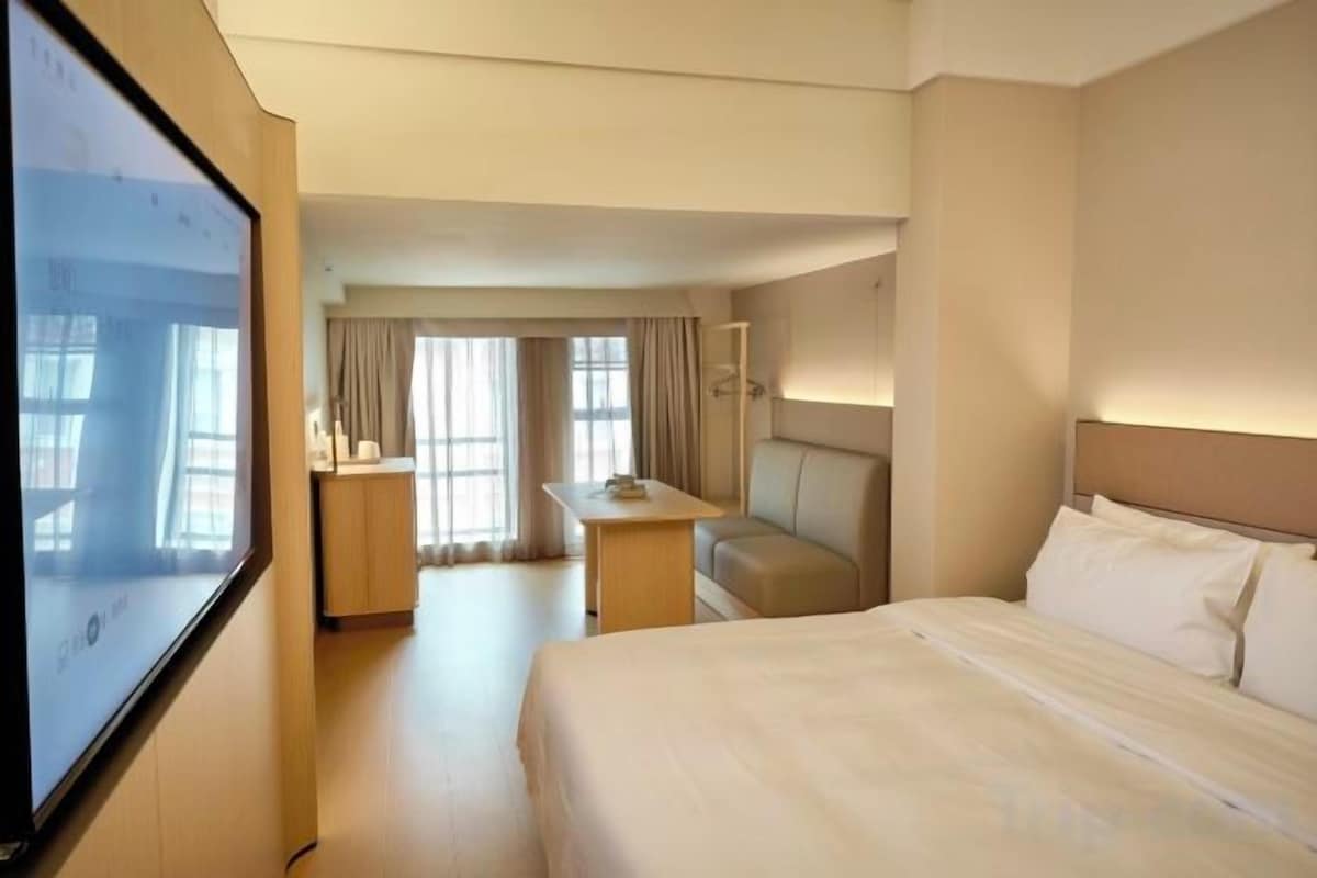 A hotel room with a bed, a desk, a chair, and a television.