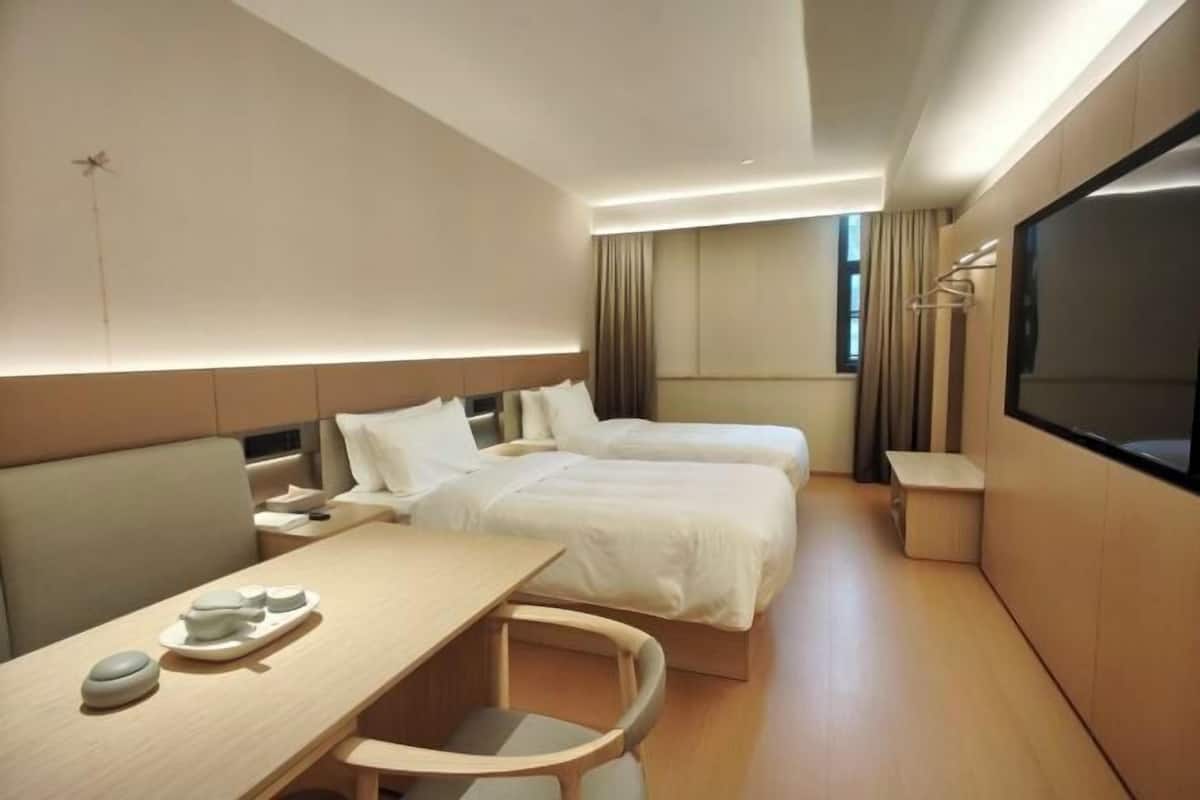 A hotel room with two beds, a desk with a chair, a TV, and a window with curtains.