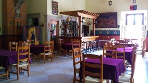 Un restaurante con sillas y mesas de madera, una zona de bar y un mural en la pared.