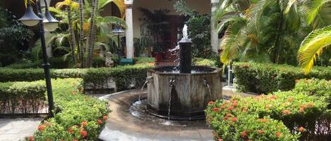 Une cour intérieure avec une fontaine centrale, entourée de haies bien entretenues et de plantes en fleurs.