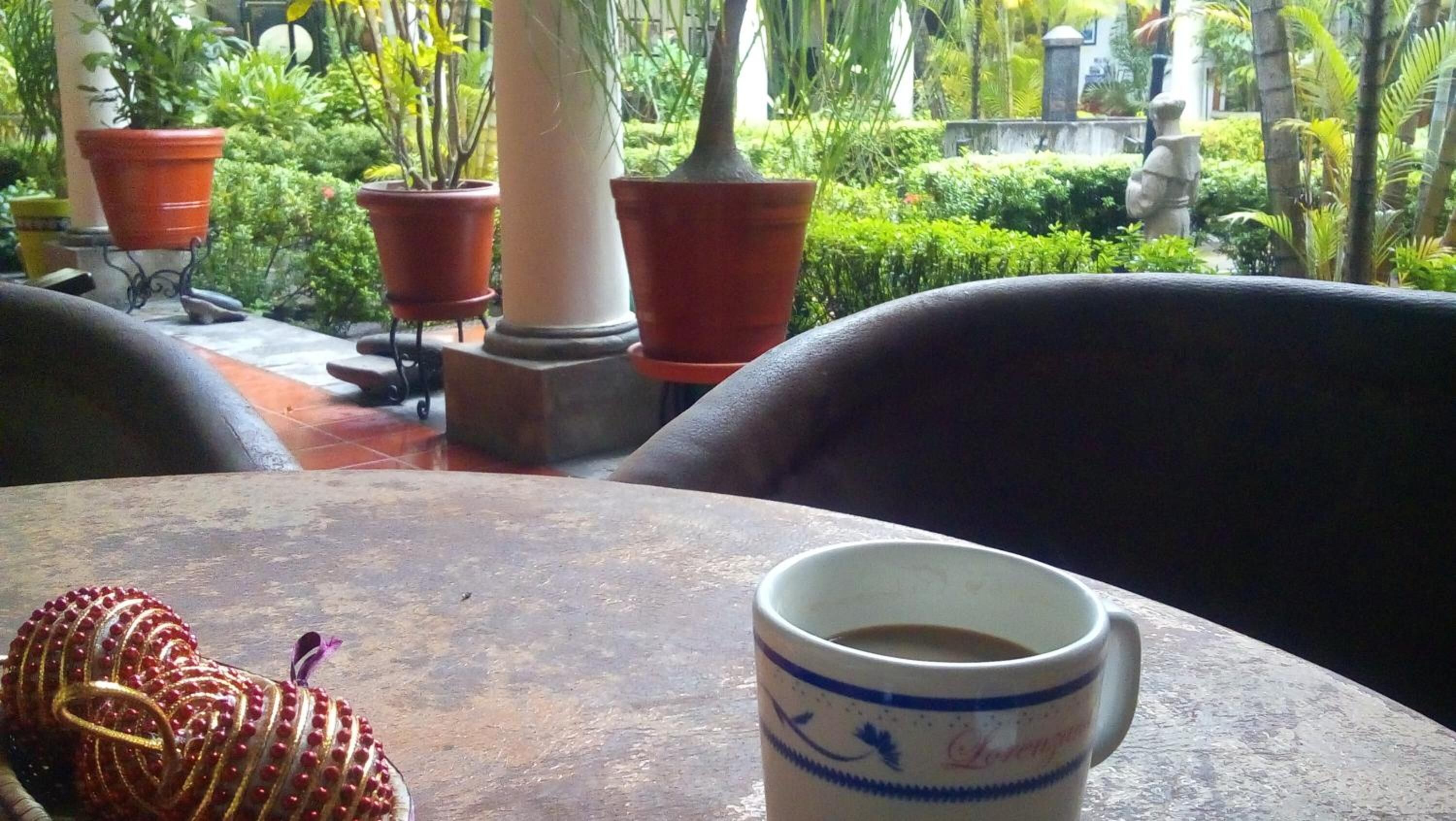 Una mesa con una taza y un adorno, rodeada de plantas en macetas y un pilar de piedra.
