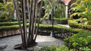A courtyard with a fountain, palm trees, and a red building with arches. - Hotel Hacienda Flamingos (San Blas)