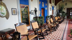 A hotel lobby with rows of wooden chairs, a patterned floor, and various wall decorations including framed pictures and a mirror. - Hotel Hacienda Flamingos (San Blas)