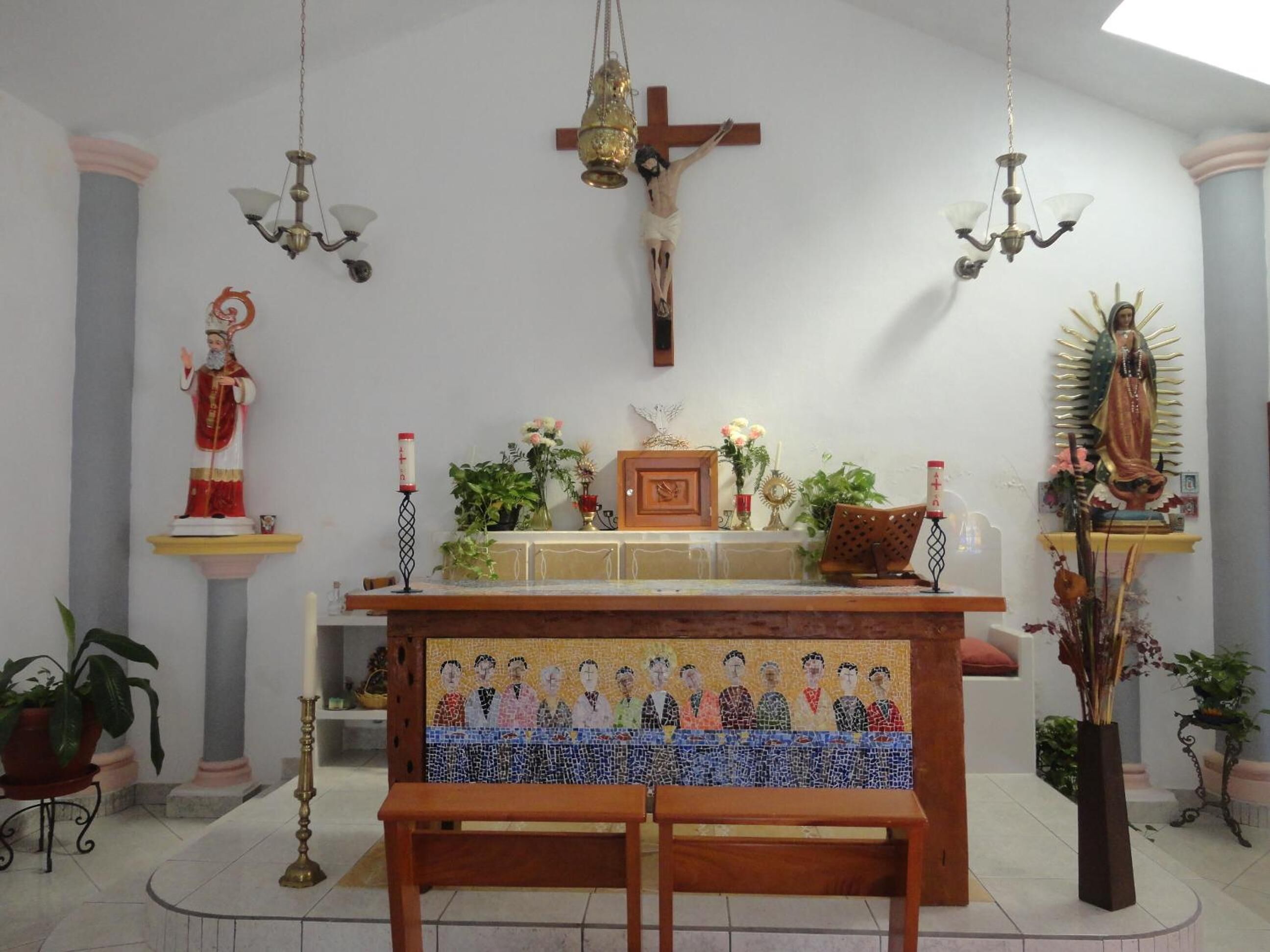 L’intérieur d’une église, avec un autel en bois, des statues religieuses et une mosaïque représentant un groupe de personnes.