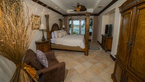 A bedroom with a four-poster bed, a sitting area with a brown sofa, a television, and a large wooden cabinet. - Los Suenos Resort Marbella 3D (Jacó)