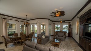 A spacious living room with a large sofa, a dining table, and chairs, a ceiling fan, and a television. - Los Suenos Resort Marbella 3D (Jacó)