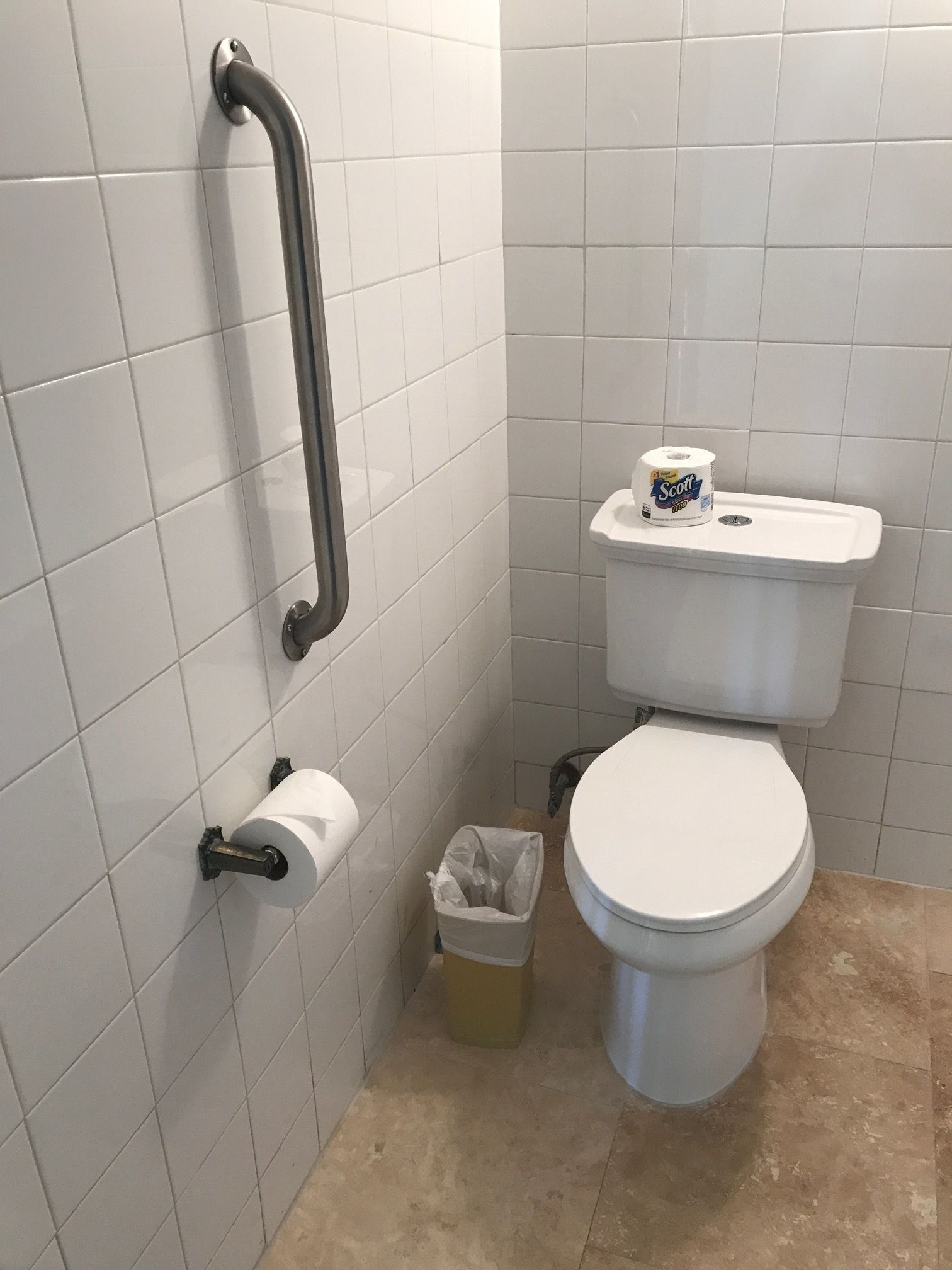 Un baño con azulejos blancos, un inodoro, un pasamanos y un cubo de basura.