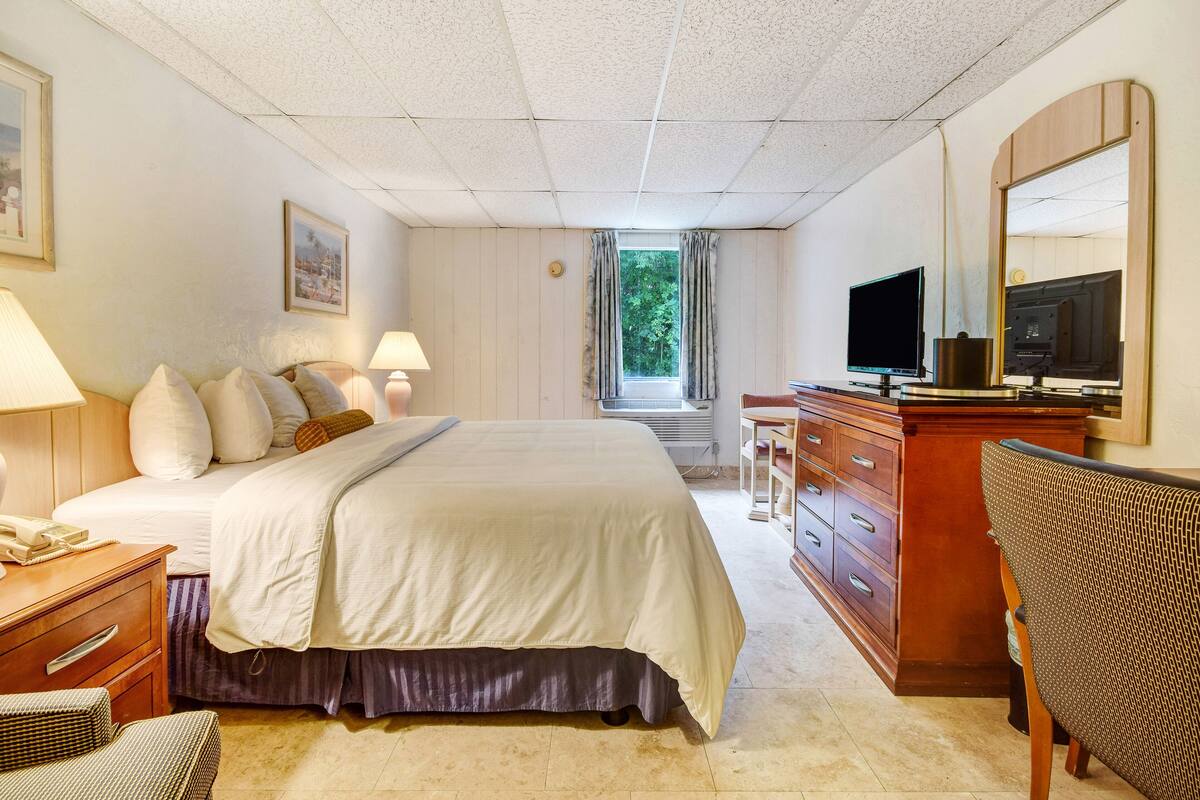 A hotel room with a bed, bedside lamps, a desk with a television, a chair, and a large mirror.