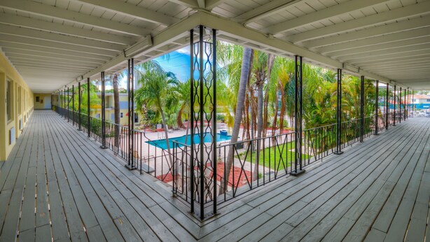 A covered outdoor area with a pool, palm trees, and a wooden deck.
