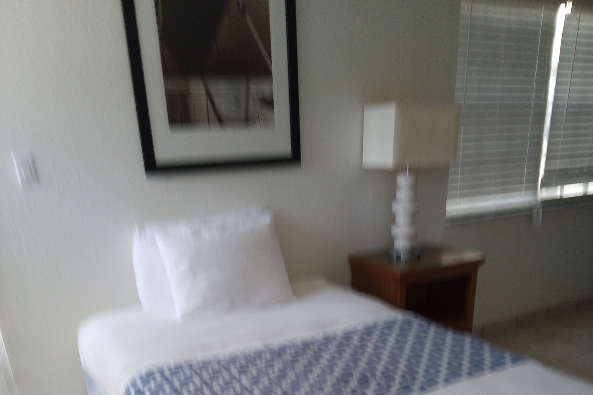 A neatly made bed with a patterned bedspread, a white pillow, and a wooden nightstand with a lamp.