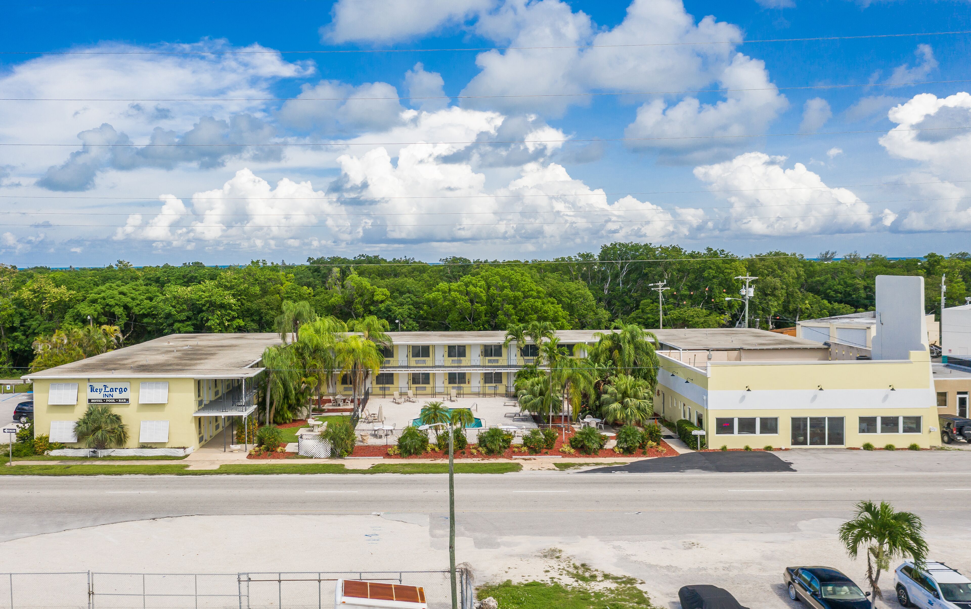 Un motel composé d’un bâtiment à deux étages, d’un parking et dont l’arrière-plan est constitué d’un luxuriant feuillage verdoyant.