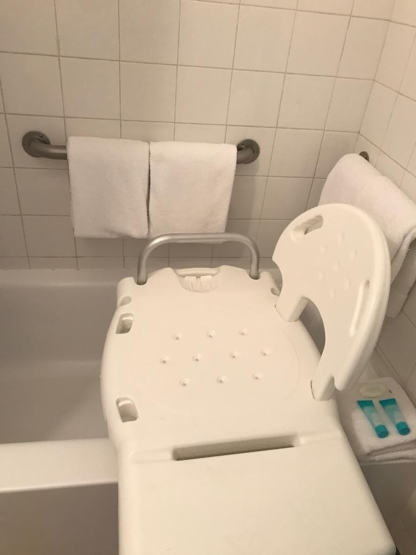 Une baignoire dotée d’un siège blanc et de barres d’appui, une serviette blanche accrochée au mur et un panneau de commande avec des boutons.