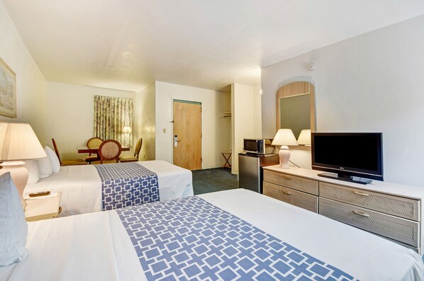A hotel room with two beds, a desk, a chair, a television, and a dresser.