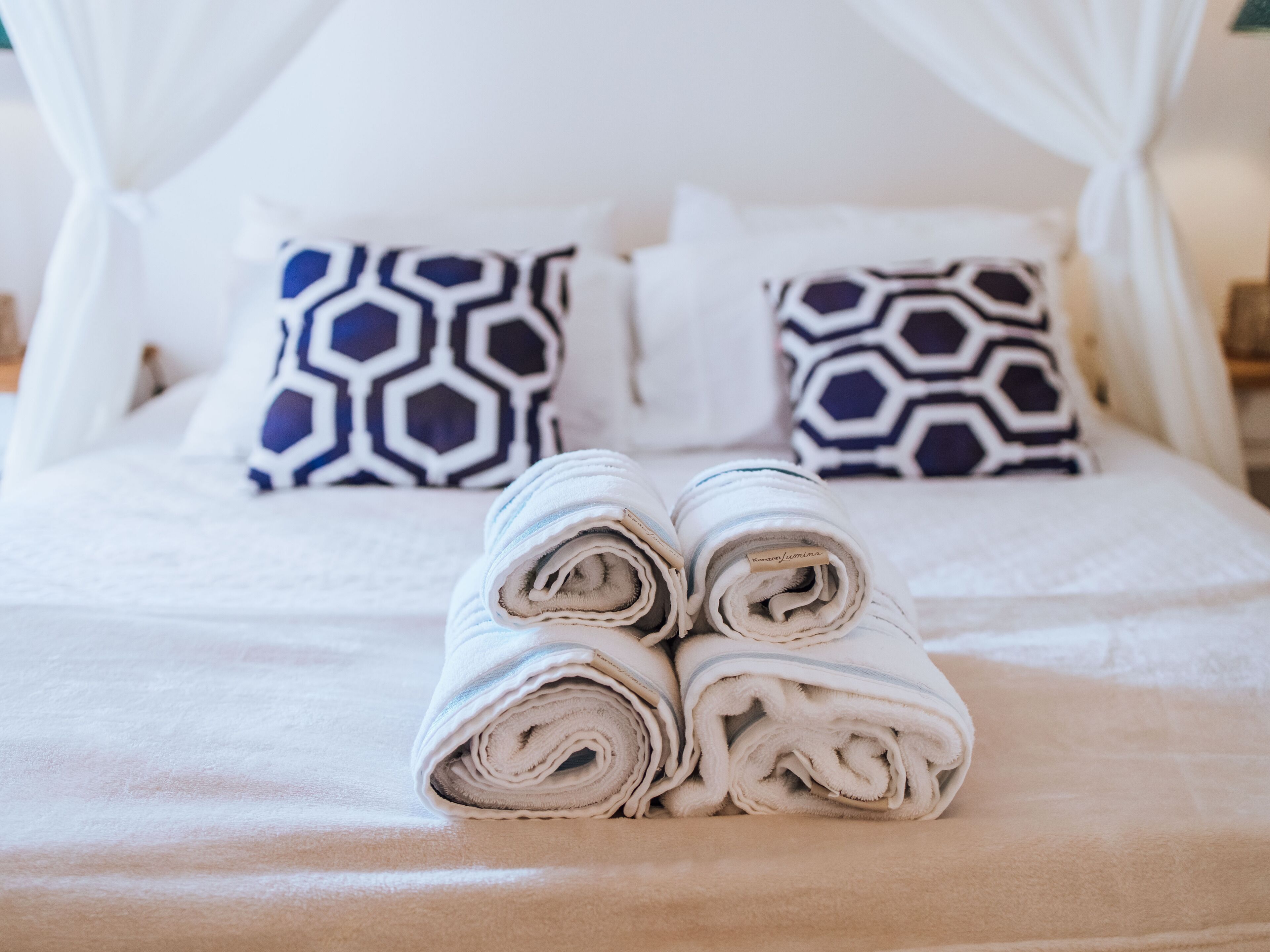 Een opgemaakt bed met opgerolde handdoeken, een hemelbed en gestreepte kussens.