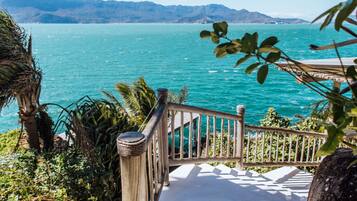 A wooden staircase leading to a balcony overlooking a turquoise sea with distant mountains.
