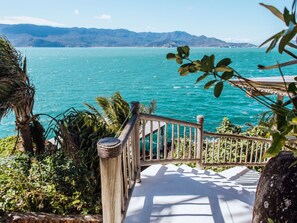A wooden staircase leading to a balcony overlooking a turquoise sea with distant mountains. - Vilatoro Guest House (Ilhabela)