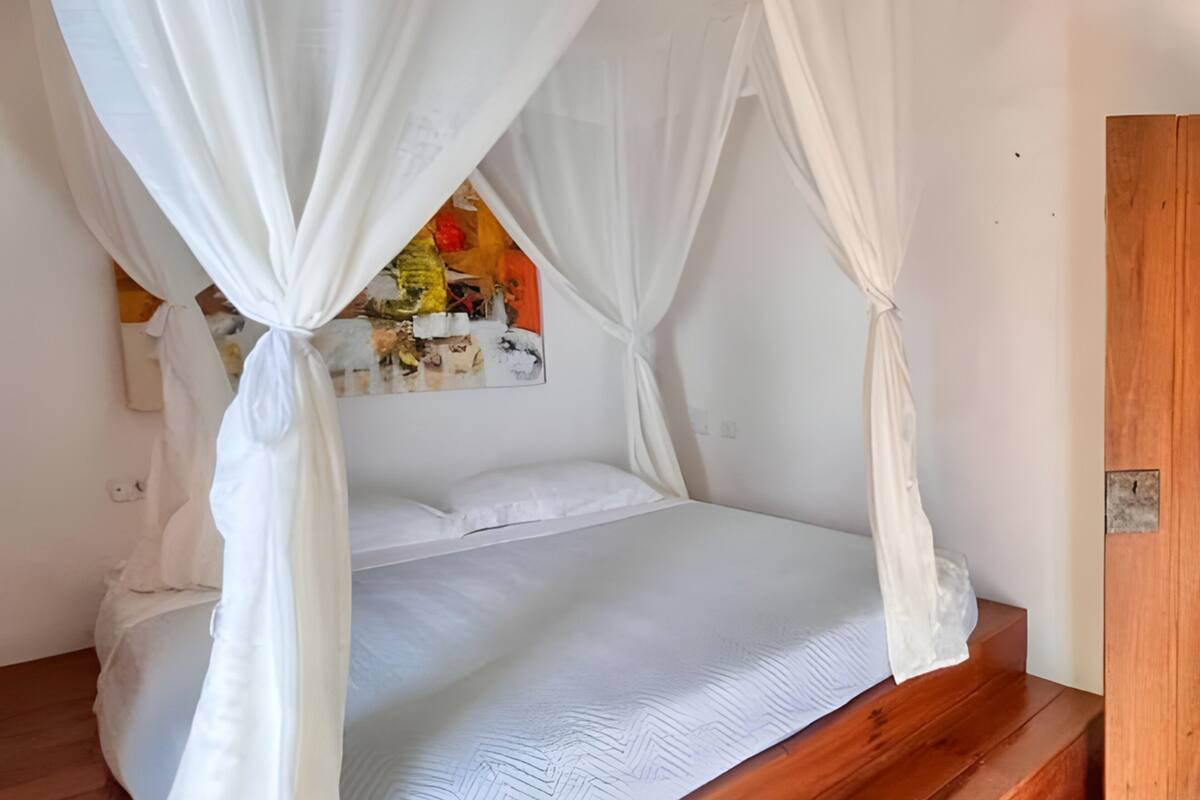 Un dormitorio con cama a dosel, suelo de madera, una lámpara de pared y una puerta.