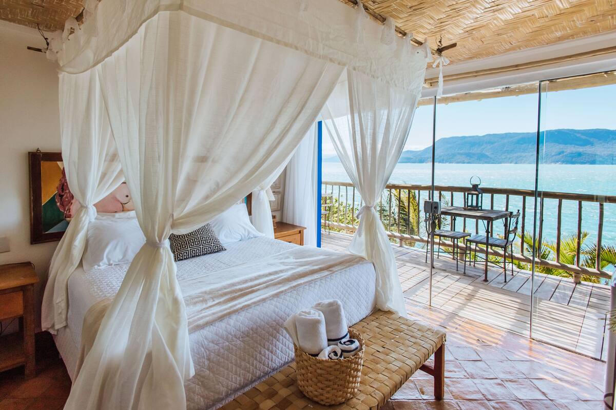 Un dormitorio con cama con dosel, vista al mar y terraza de madera.