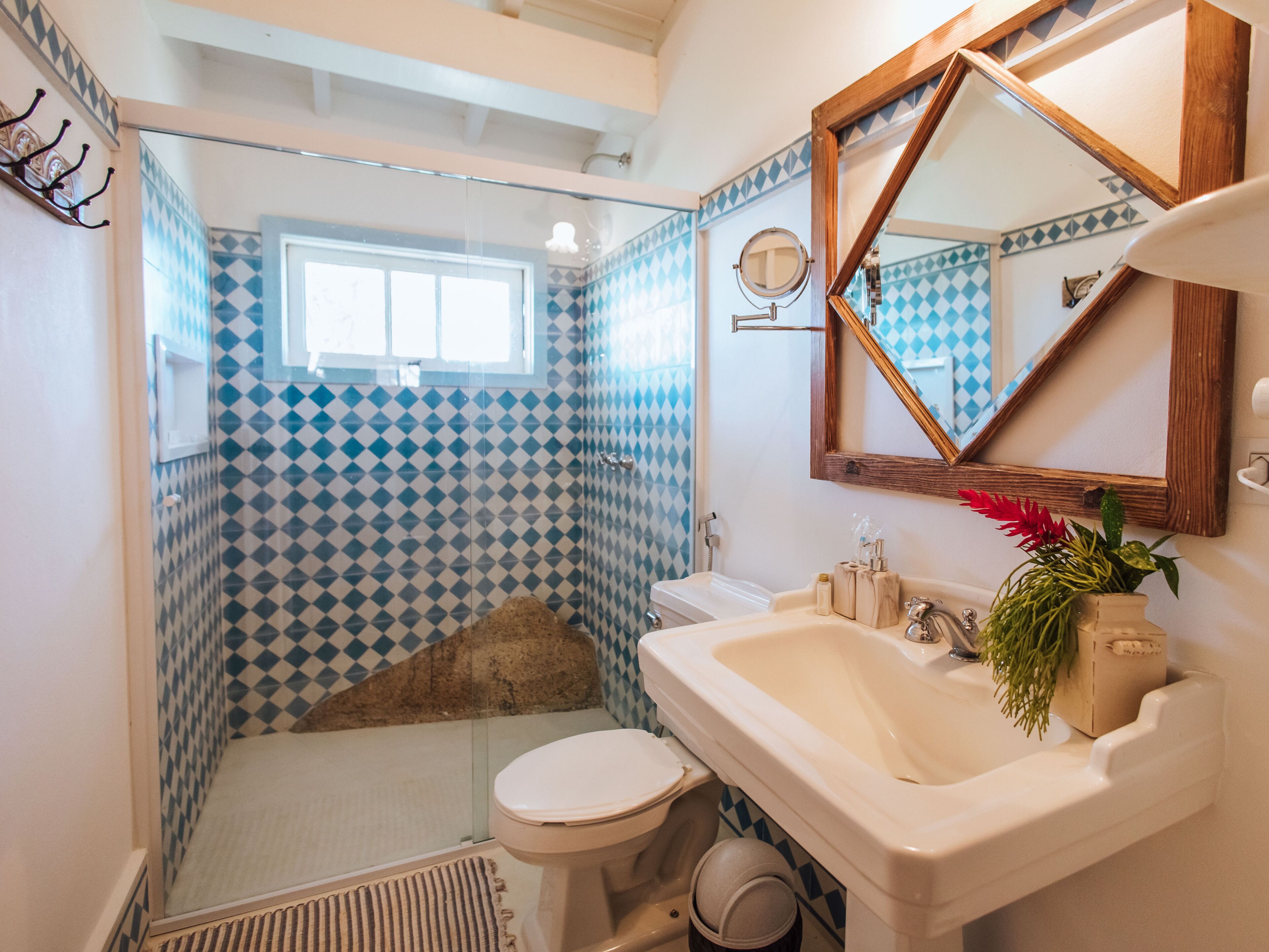 Une salle de bain avec un mur recouvert de carreaux aux motifs géométriques, un lavabo blanc avec un miroir au-dessus, et un espace douche.