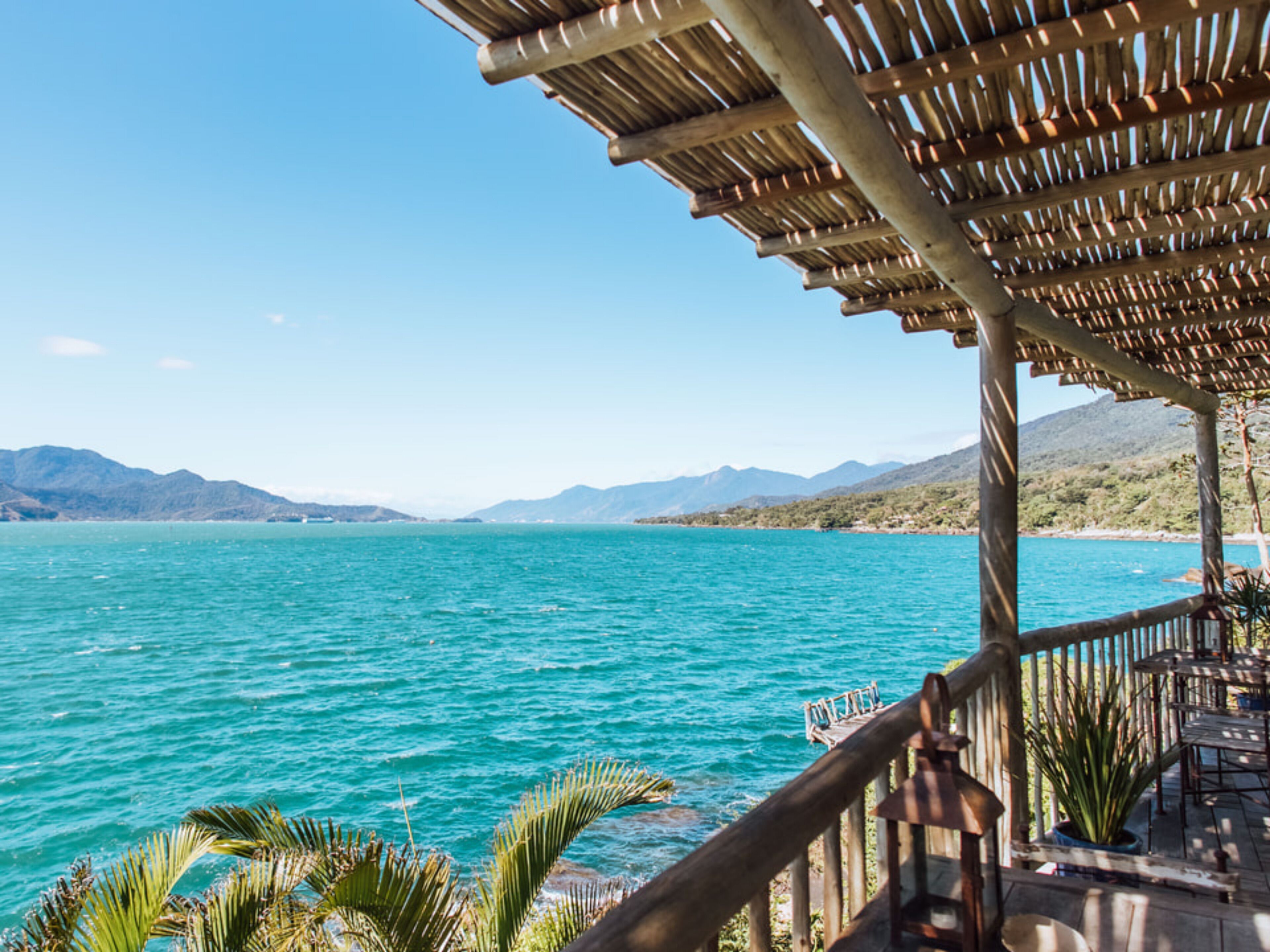 A seaside view with a wooden deck, palm trees, and a clear sky.