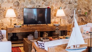 Ein Wohnzimmer mit Steinwand, Fernseher, zwei Lampen, einem Holztisch und einem Modell eines Segelboots.